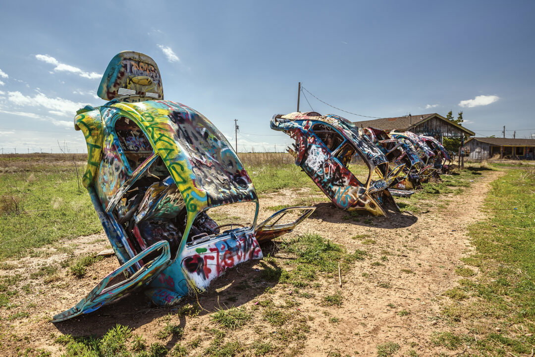 A bunch of graffitied Volkswagen Beetles stuck into the ground.