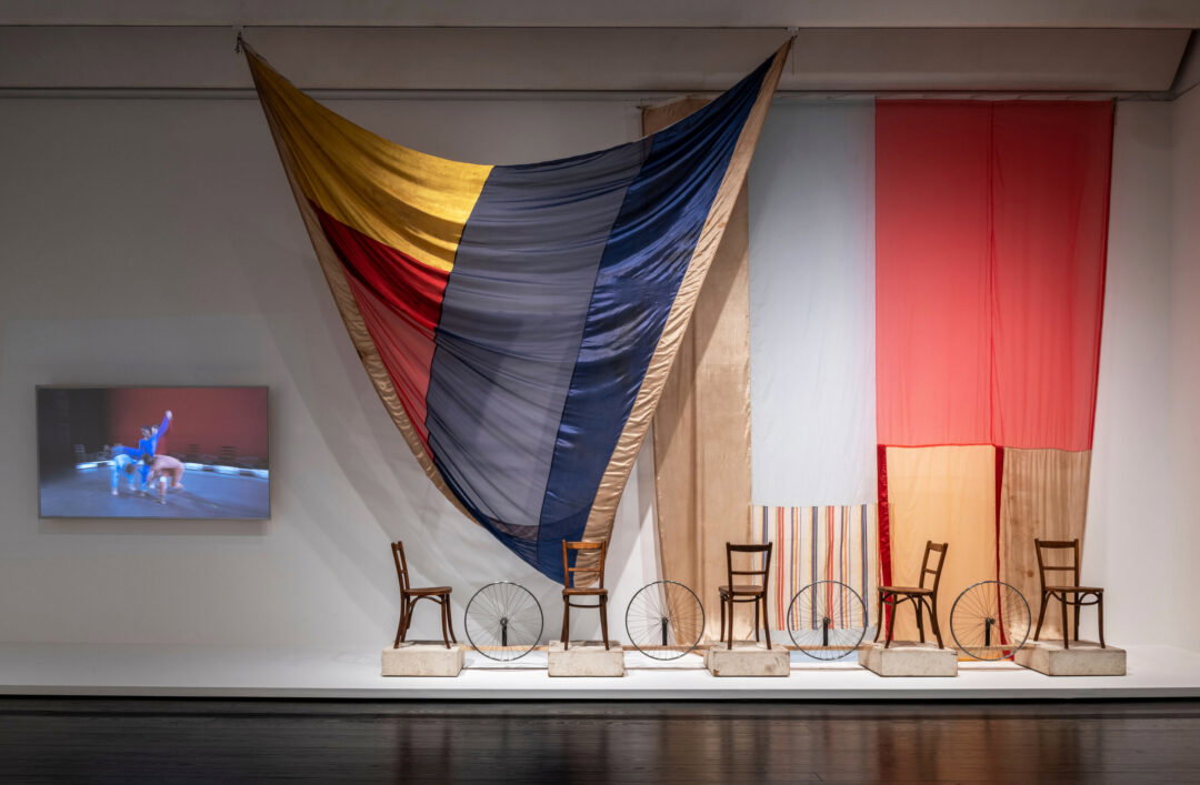 A fabric work with chairs and a dance video on display at an art museum.
